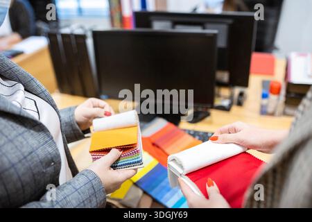 Two designers or a client and a decorator collaborating on a project. They are choosing from a variety of colorful fabric swatches for fashion or inte Stock Photo