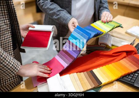 Two designers or a client and a decorator collaborating on a project. They are choosing from a variety of colorful fabric swatches for fashion or inte Stock Photo