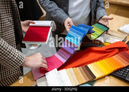 Two designers or a client and a decorator collaborating on a project. They are choosing from a variety of colorful fabric swatches for fashion or inte Stock Photo