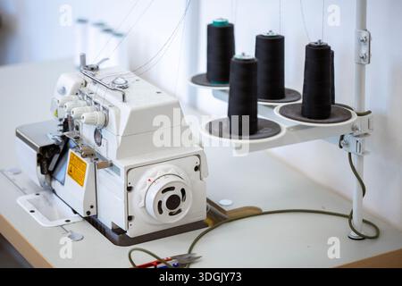 A professional overlock sewing machine, or serger, with black thread spools in a garment factory. A concept of the textile industry, tailoring, and cl Stock Photo