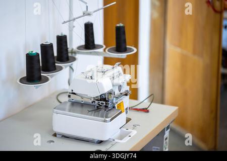 A professional overlock sewing machine, or serger, with black thread spools in a garment factory. A concept of the textile industry, tailoring, and cl Stock Photo
