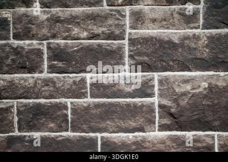 A high-resolution texture of a traditional dark basalt or sandstone block wall with white mortar. Stock Photo