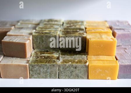 Various bars of handmade, cold-process soap are curing on a shelf. These organic cosmetics feature different natural ingredients, resulting in beige, Stock Photo