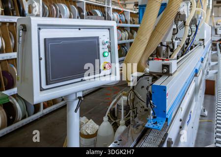 A close-up of the edge banding machine's control panel. The touchscreen HMI operates the automated system in a modern furniture factory, with the conv Stock Photo