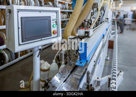 A close-up of the edge banding machine's control panel. The touchscreen HMI operates the automated system in a modern furniture factory, with the conv Stock Photo
