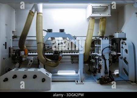 A wide view of the internal mechanics of a automatic edge banding machine in a furniture factory. It shows the rollers, motors, and yellow corrugated Stock Photo