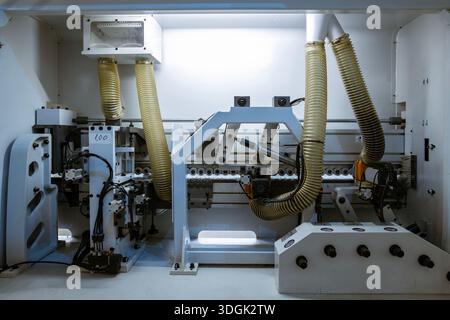 A wide view of the internal mechanics of a automatic edge banding machine in a furniture factory. It shows the rollers, motors, and yellow corrugated Stock Photo