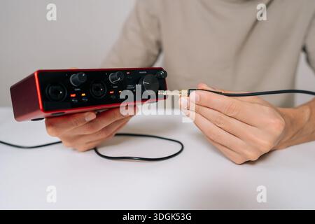 Person hands connecting audio jack cable into red usb audio interface, preparing for home music production, recording, and sound engineering in Stock Photo