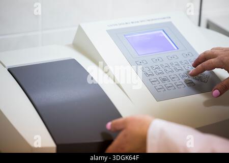 Close up view of a scientist hand pressing buttons on the control panel of a modern UV VIS double beam spectrophotometer device during chemical resear Stock Photo