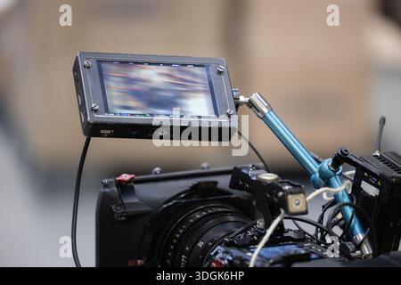 A professional on-camera field monitor is mounted on a digital cinema camera rig. Below, the camera body and a compact prime lens are visible. The beh Stock Photo