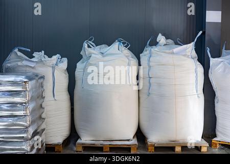 Three large white woven bulk bags (FIBC) stand on wooden pallets in a modern warehouse. The bags are filled with industrial powder or granules. A pall Stock Photo