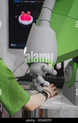 Woman and humanoid robot arm with articulated fingers above computer desk in modern tech workspace, working together, pregaming and operating  Stock Photo
