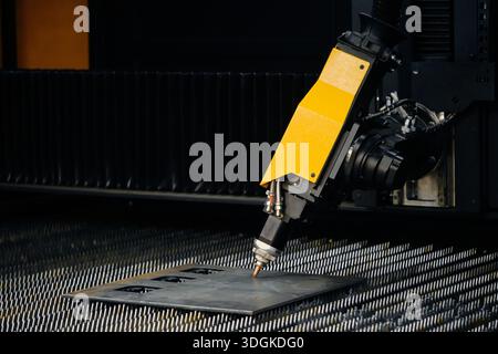 Close-up of fiber laser cutter nozzle and head assembly during high-speed sheet metal profile cutting on CNC flatbed table Stock Photo