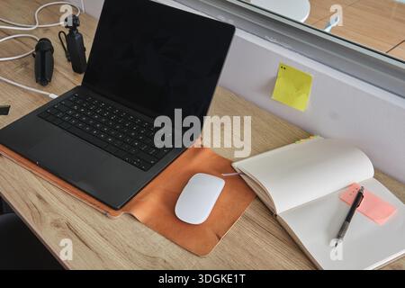 Workspace with a laptop, mouse, notebook, and pen on a wooden desk, reflecting productivity Stock Photo