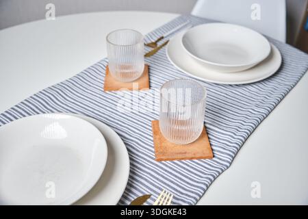 Dining table set for two with plates, glasses, and a striped table runner Stock Photo