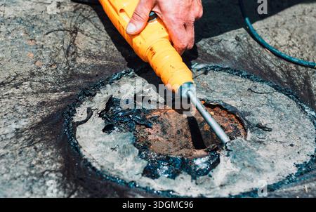 Worker using a rotary hammer drill to break up concrete or asphalt surrounding a utility access point. Person uses power tool to break concrete Stock Photo
