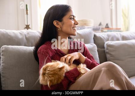 Happy young Indian woman holding cute sleepy ginger cat Stock Photo