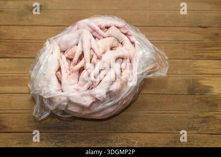 Raw chicken feet in a plastic bag on a wooden background. Raw chicken feet stacked inside a clear plastic bag. Stock Photo