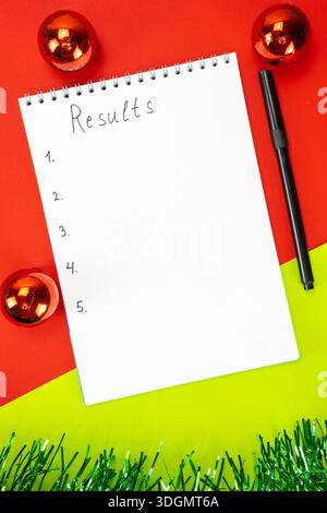 Three New Year's red balls and a notebook with the results of the year on a red Christmas background. New Year's decoration. Stock Photo