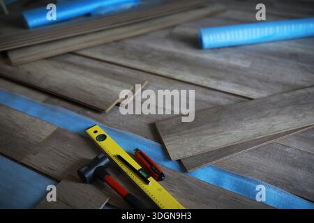 Installing laminated floor, detail on man hands holding wooden tile, over white foam base layer, small pile with more tiles background Stock Photo