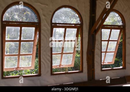 Three wooden arched window frames open outward on white textured wall revealing green garden nature view creating peaceful calm atmosphere inside brig Stock Photo