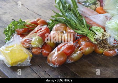 Fresh organic tomato and spring onion packed in clear plastic bag with yellow butter on rustic wooden table background showing healthy vegan ingredien Stock Photo