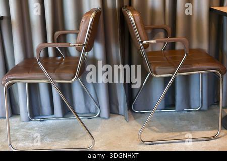 Side view of two vintage brown leather chair and metal frame with modern style located in living room giving cozy and comfort feeling with grey curtai Stock Photo