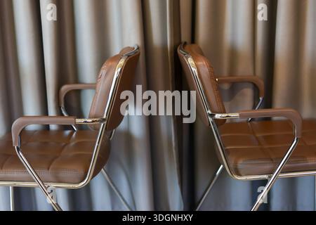 Quiet brown leather chair pair facing beige curtain background creating professional formal mood in modern office interior empty seat furniture design Stock Photo