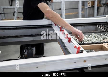 Production area for metal-plastic or PVC windows, commonly known as vinyl windows. A worker is installing locks onto a window frame using red clamps a Stock Photo