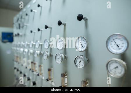 Control panel with multiple pressure gauges and adjustment knobs used for regulating fluid or gas pressure in an industrial system. The gauges display Stock Photo