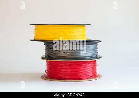 Yellow, gray, and red plastic filaments for 3D printing on spools on a white background, 3D printer material, raw materials for manufacturing and prin Stock Photo