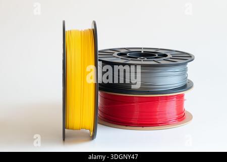 Yellow, gray, and red plastic filaments for 3D printing on spools on a white background, 3D printer material, raw materials for manufacturing and prin Stock Photo