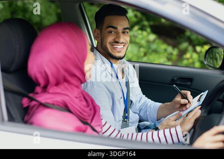 Driving School Test. Handsome Young Arab Instructor Examining Muslim Female Drive Stock Photo
