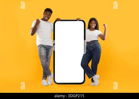 Two People Stand Next to a Large Empty Smartphone Display on a Bright Yellow Background Stock Photo