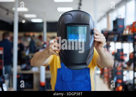 A man in a workwear wearing a protective welding helmet inside a store Stock Photo