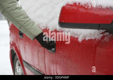 Person struggles to unlock a frozen car door handle covered with ice and snow Stock Photo