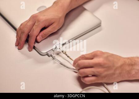 Repairing laptop power cord, Detailed image of fixing broken laptop charger wire, Closeup of skillful person restoring worn electrical cord for Stock Photo