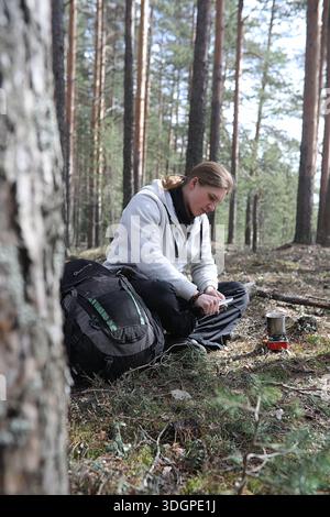 A man in a campaign drinks tea. A young traveler in the woods camped and cooked breakfast in nature. The naturalist drinks hot fresh tea cooked on ope Stock Photo