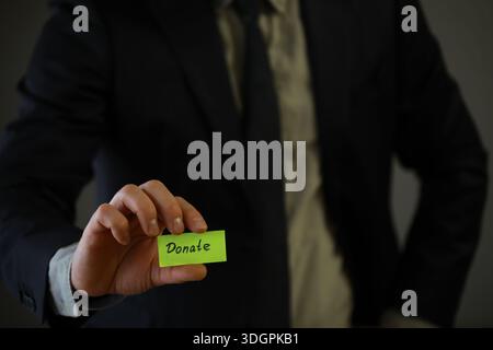 Businessman shows a wooden block with the word donate. Charitable donation in business concept. Stock Photo