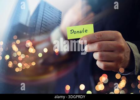Businessman shows a wooden block with the word donate. Charitable donation in business concept. Stock Photo