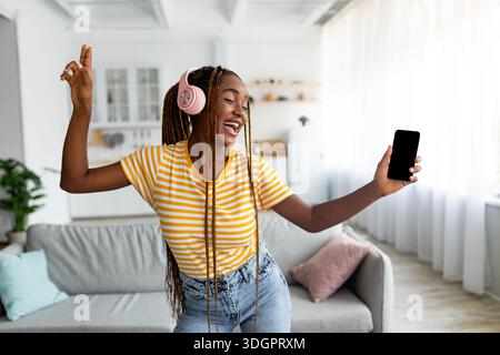 Joyful afro american long-haired woman singing and dancing, using smartphone Stock Photo