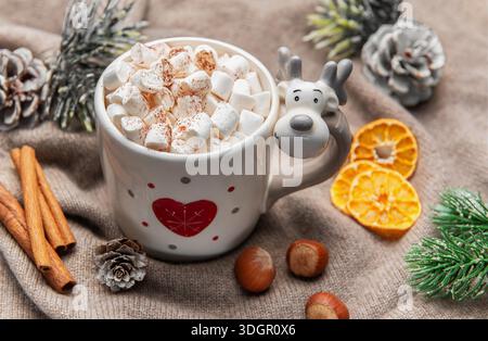 Cozy winter drink in a festive reindeer mug with pine cones and cinnamon sticks Stock Photo