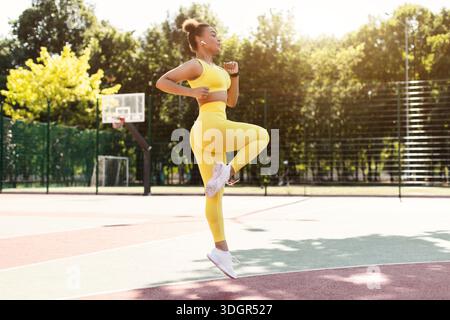 Sporty black woman in yellow sportswear jumping and running Stock Photo