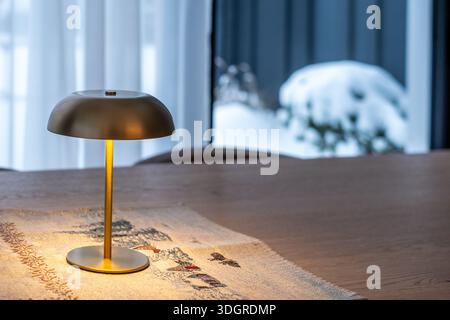 Riga, Latvia - January 02, 2026: Rechargeable table lamp from Zara home emits warm light on wooden table, with a Stock Photo