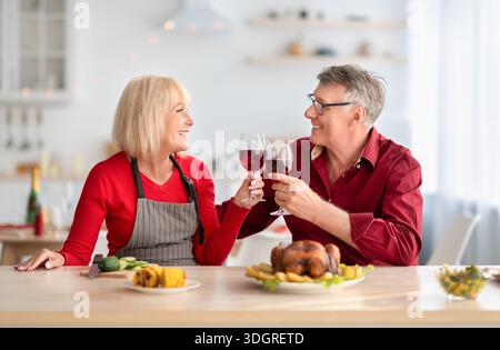 Senior couple having romantic times, drinking red wine while cooking festive Thanksgiving or Christmas dinner at kitchen Stock Photo