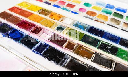 White plastic box with watercolor paints. Opened paint set for professional watercolor painter on white background. Used paint collection close up Stock Photo