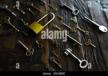 A lot of metal keys and a steel lock on a wooden boards. Vintage rusty padlock surrounded by old keys. Security or secret protection concept. Internet Stock Photo
