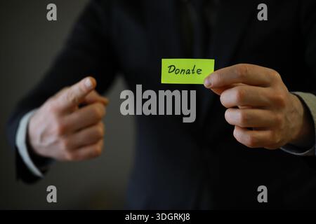 Businessman shows a wooden block with the word donate. Charitable donation in business concept. Stock Photo