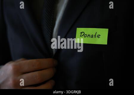 Businessman shows a wooden block with the word donate. Charitable donation in business concept. Stock Photo