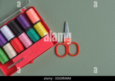 Sewing supplies spools thread, needles and scissors in red box on green background, top view Stock Photo